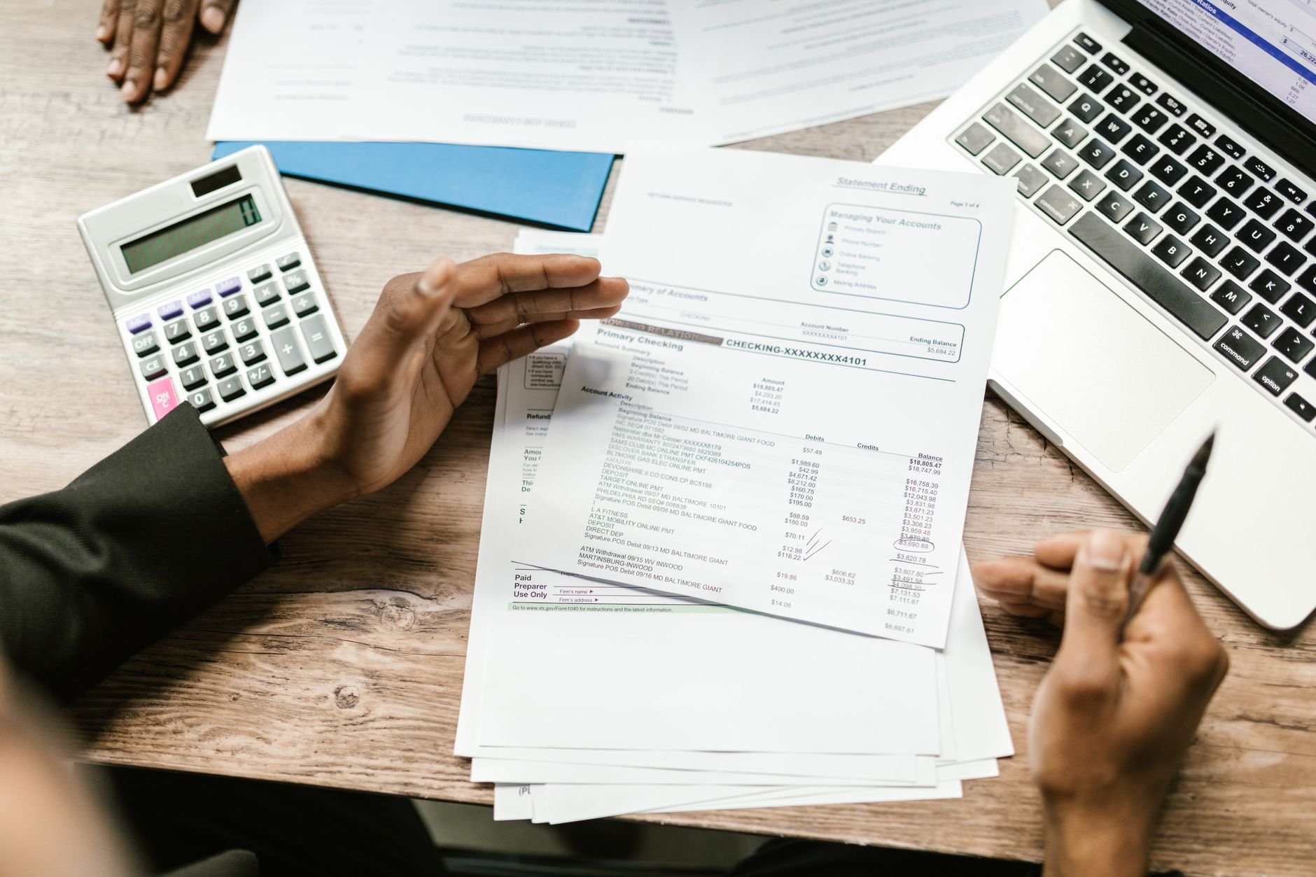 Hands holding financial documents with calculator and laptop on office desk.
